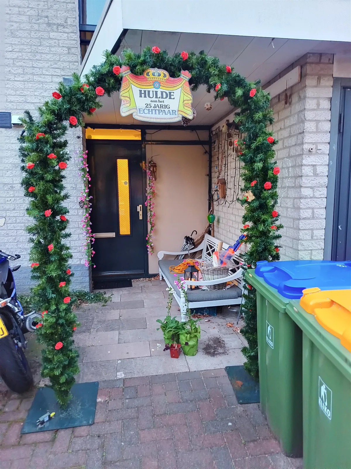Volledige groene ereboog met rode rozen en twee vlakke voeten bij een voordeur